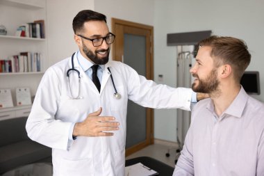 Destekleyici sağlık hizmeti iletişimi. Gülümseyen dost canlısı genç doktor hasta ile etkileşim halinde. Omuz omuza vererek özen göstermeyi teşvik etti. İyileşmeye duyulan güveni ifade etti.