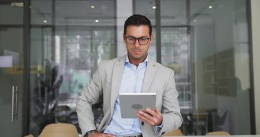 Ciddi bir online ürün yöneticisi, gözlüklü adam tablet kullanıyor, ofiste tek başına duruyor, başka tarafa bakıyor, satış büyümesi için geliştirme stratejisi düşünüyor, problem çözüyor.