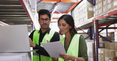 Birlikte envanter yapan, kağıt sevkiyatı yapan, dizüstü bilgisayarda yazan, metal raflardaki farklı kutuları gösteren, konuşan, gülümseyen Latin iş arkadaşları.