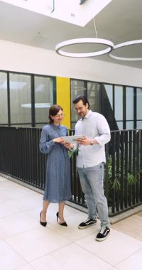 Çevrimiçi projeyi tartışan iki erkek ve kadın meslektaşım dijital verileri inceliyor, iş stratejisi geliştiriyor, şirket koridorunda duran tableti kullanarak takım çalışması sırasında bilgi araştırıyor.