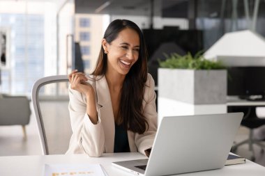 Modern ofiste dizüstü bilgisayar kullanan, gülen genç profesyonel bir kadın, hoş iş haberleri okuyor, ticari teklif veya fırsat alıyor, iş saatlerinde mola veriyor, çevrimiçi eğlenceli içerikler izliyor