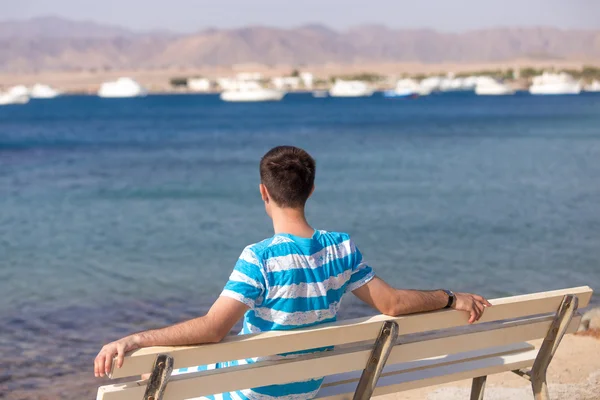 Young man relaxing on bench on the beach — Stock Photo, Image