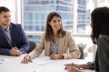Resmi giyimli profesyonel orta yaşlı kadın, iş ortaklarıyla konferans masasında oturur, güven yayar, kalem tutar, kontrat imzalamaya ya da anlaşma imzalamaya hazırdır. Birleşme, ticari anlaşma.