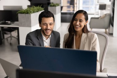 İki mutlu takım üyesi masada oturmuş memnun bir gülümsemeyle bilgisayar monitörüne bakıyor, sunum hazırlıyor, şirket ofisindeki ara sırasında eğlenceli içeriği izliyor. Takım çalışması, teknolojiler, yenilikler