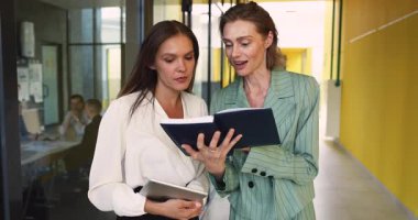 İki iş kadını şirket iş birliği ofisinde birlikte duruyorlar, not defterindeki notları gözden geçirdikten sonra tokalaşıyorlar ve proje detayları tartışıyorlar. Planlama desteği, takım çalışması, verimli karar verme