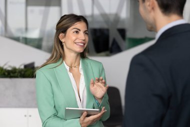 Gülümseyen, kendine güvenen İspanyol iş kadını elinde dijital tablet bulunan güvenilir bir uzman, erkek müşteri veya iş arkadaşıyla görüşüyor ve danışmanlık yaparak satış önerisini açıklıyor, profesyonel tavsiyelerde bulunuyor.