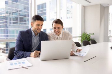 İki gülümseyen takım üyesi konferans masasında oturmuş laptopa bakıyor, iş verilerini inceliyor, mali raporları inceliyor, sunum ve slaytları tartışıyor, verimli bir takım çalışmasıyla tatmin oluyor.