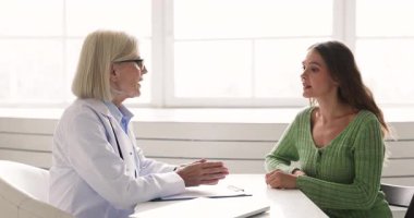 Beyaz önlüklü kadın doktor masada oturuyor ve klinikte muayene sırasında kadın hastaya tıbbi sonuçları, teşhisi ve tedavi seçeneklerini açıklıyor. Profesyonel sağlık hizmetleri