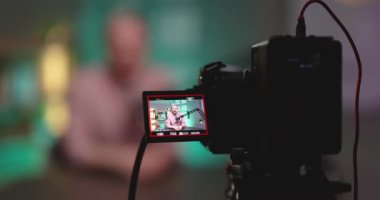 Video çekimi sırasında dijital kamera görüntüsünü kapat. Mikrofon ve bulanık arka plandaki ışıklarla profesyonel stüdyo kurulumu sırasında podcast sunucusunu yakala. Video üretimi ve podcast kayıt süreci