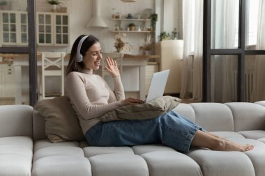 Mutlu genç kadın evdeki kanepede oturarak video görüşmesi yapıyor, kulaklık takıyor arkadaş ya da aile toplantısını laptopuyla başlatıyor. Sanal buluşma olayı, teknoloji, uzaktan konuşma konsepti