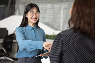Neşeli genç Asyalı yönetici kadın bayan patrona, meslektaşına el sıkışırken kariyer terfisi, profesyonel başarı ve mülakat üstüne iş bulmaktan dolayı tebrik alıyor.