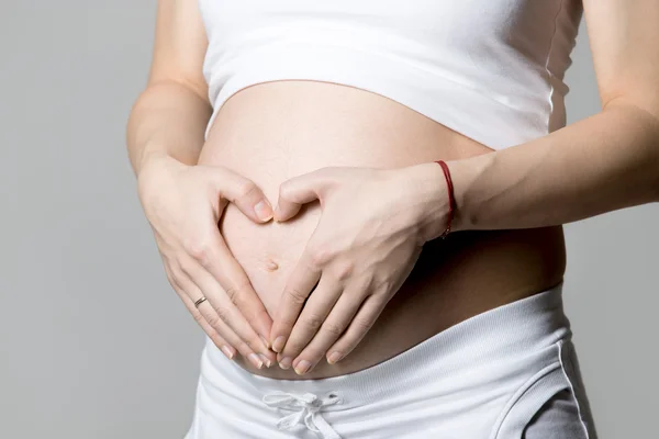 Pregnant woman showing heart shape on her belly — Stock Photo, Image