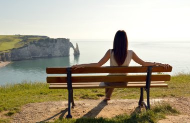 Etretat, Normandy, Fransa için bir uçurumun üstünde bir bankta oturan genç kadın.