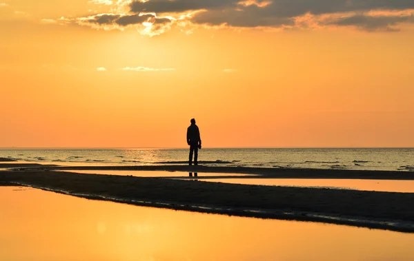 Silueta muže sledovat západ slunce na pobřeží — Stock fotografie
