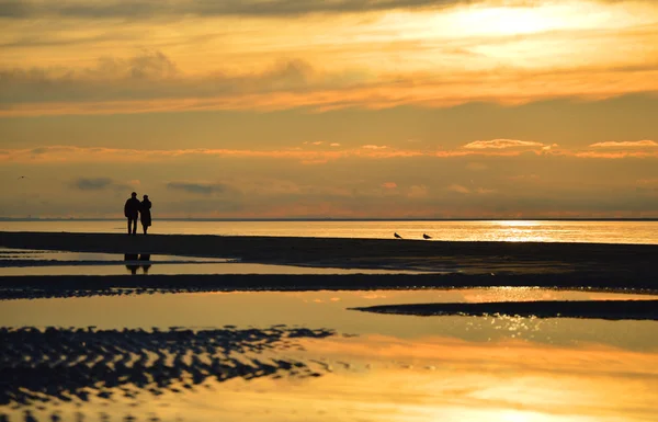 リガ、ラトビアの夕日、浜辺に沿って歩いてカップルのシルエット — ストック写真