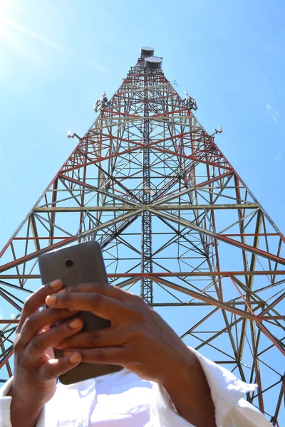 Mulher segurando um smartphone perto da torre de telecomunicações — Fotografia de Stock