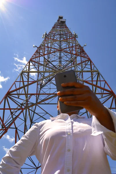 Nő egy smartphone gazdaságban, távközlési torony közelében — Stock Fotó