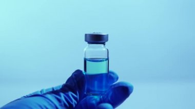 COVID-19 konseptine karşı aşı. Laboratuvar bilim adamı steril şişeyi mavi antivirüsle tutuyor. Coronavirus 'un solunum sendromunun tedavisini arıyorum. Tasvir araştırmasında dünya yarışı.