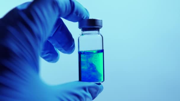 Mano de científicos en guantes azules sosteniendo el vial con una vacuna segura y eficaz contra el virus. Concepto de investigación y aprobación de la cura en el laboratorio. — Vídeo de stock