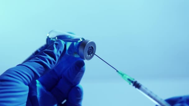 Arts of verpleegkundige handen die vaccin of medicatie toedienen met spuit en blauwe vaccinflacon in het ziekenhuis. Gezondheids- en medische begrippen. Vulspuit uit glazen fles. — Stockvideo