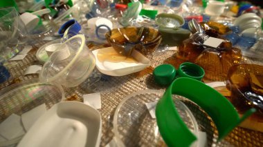 Evdeki plastik çöpler masanın üzerinde. Atıklar atıldı, denizciden toplandı. Plastikten yapılmış şehir çöplüğü. Boş şişe ve bardaklar çevresel kirlilik ve ekolojik sorun yaratıyor.