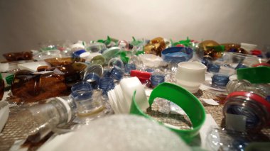 Plastik şişe parçaları, bardaklar, mantarlar, pipetler, su ve şampuan şişeleri, krem ambalajlar ve masaya atılan diğer bir kerelik çöpler. Çevre kirliliği, geri dönüşüm, atık yönetimi sorunu.