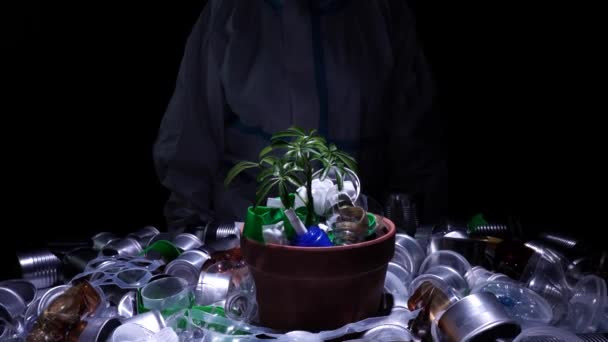 Miljöaktivist i skyddsdräkt håller unga plantor i kruka full av plast smuts skräp. Begreppet och symbolen för katastrofal apokalyps, ekologisk hållbarhet, tillväxtvård, skydd av jorden. — Stockvideo