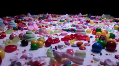 Şekerleme masasında çok renkli şeker topları. Çikolata kaplı ve jöleli şekerlerden oluşan şekerleme arka planı. Çeşitli şekillerde lezzetli şekerlemeler. Tatil festivali arka planı.