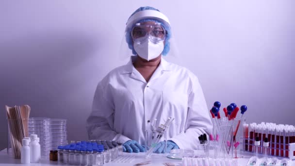 白いパイプスーツを身に着けている女性看護師科学者の肖像画 医療保護スクラブ眼鏡 シールドと青い手袋で顔のマスク コロナウイルスパンデミックCovid 診療所での予防接種 — ストック動画