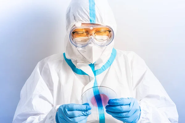 Vaccine researcher with protective clothing in the laboratory with microscope slides and Covid 19 positive blood. Lab technician with a blood sample with a new Coronavirus mutation or variant.