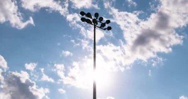 Gün batımı ve yaz bulutlarına karşı bir futbol stadyumunun ışık kulesiyle zaman geçirmek. Sinema gibi hızlı ve pürüzsüz bir gökyüzü hareketi. Futbol stadyumunun el fenerleri ve akşam süreleri.,