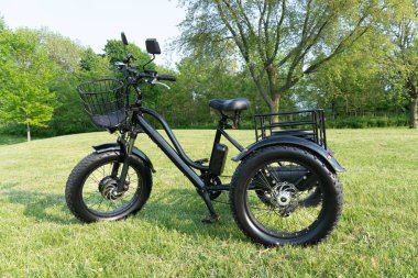 Güneşli yaz gününde parkta elektrikli trike veya e bisiklet. Yandan vurulmuş. Bir sürü ışıklandırma. Üç tekerlekli bisikletin e motor ve güç pilinin görünümü.