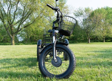 Wheel of the electric bicycle view from side. E bike motor in the park grass of the city. Unfiltered, with natural lighting, urban view. Ecology and green energy concept. EV, electric vehicle.