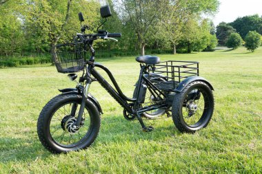 Front wheel side of the electric bicycle, view in sunny summer day in the  green grass. E bike motor with battery. Ecology and green energy concept. EV, electric vehicle.