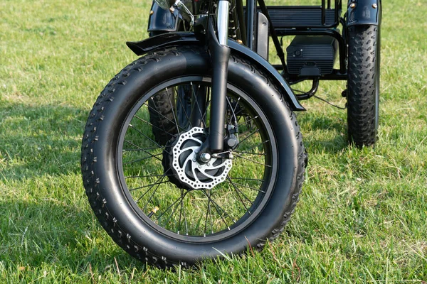 Front wheel side of the electric bicycle, view in sunny summer day in the  green grass. E bike motor with battery. Ecology and green energy concept. EV, electric vehicle.