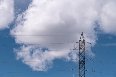 Yüksek voltajlı elektrik kulesi vericisi. Mavi gökyüzü ve bulutlu endüstriyel güç hattı.