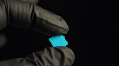 Tıbbi araştırmacılar ellerinde LSD şeritli siyah eldivenlerle Lysergic asit ilacının kuru damlasını tutuyorlar. Yakın plan çekim. Depresif hastalıkların tedavisinde ve deneylerinde kullanılan LSD