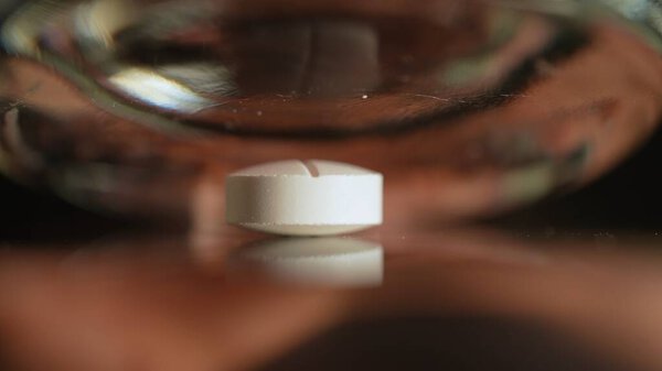 Pill crushing Into powder with kitchen glass in slow motion, extreme macro close up. Addicted people using for snorting. The medicine is crushed on the table.