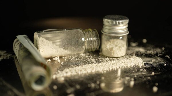 Heroin or crushed oxycodone placed in a container. Powdered illegal drugs stored in a glass vial, indicating substance abuse. Ongoing crisis involving opioids and fentanyl. 