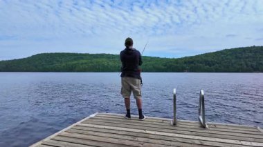 Tekne rıhtımından sakin gölde balık tutan adam olta atıyor ve makarayı kullanıyor. Yaz tatilinde balık tutan balıkçı..