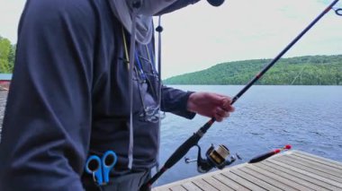 Tekne rıhtımından sakin gölde balık tutan adam olta atıyor ve makarayı kullanıyor. Spor balıkçısı UV koruyucu başlık ya da kar maskesi olarak kar maskesi kullanıyor. Balık tutma yaz tatili