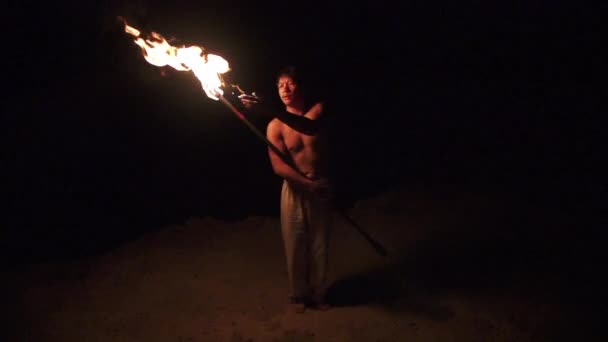 Skilled fire dancer lights fire staff using his hand then looks at camera, slow motion (60 fps) — Stock Video