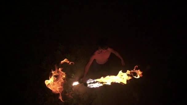 Skilled fire dancer looks up at camera, throws fire staff toward camera and catches it, performs fire spinning, top down shot, slow motion (60 fps) — Stock Video