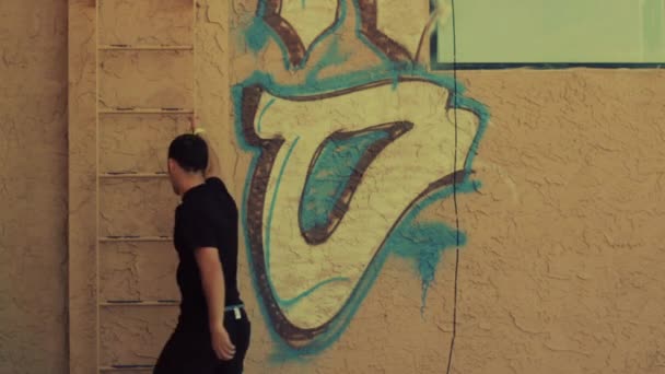 Férfi sétál fel, és majd mászik a létra graffiti fal mellett a tető — Stock videók