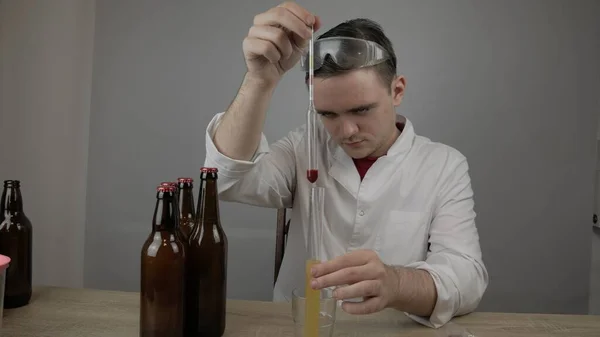 young master technologist brews beer at home, pours beer into bottles, checks the sugar level in beer, checks the percentage of alcohol in beer, checks the quality of the brewed beer