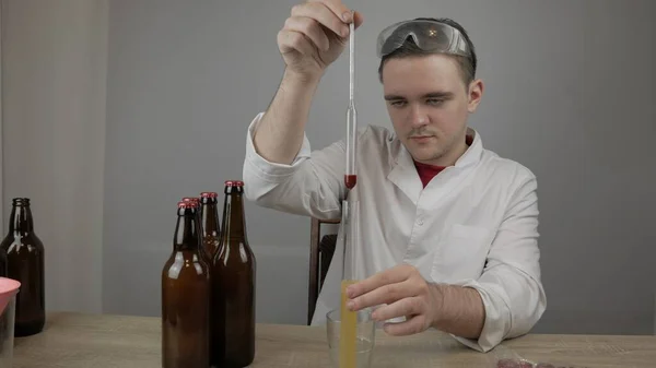 young master technologist brews beer at home, pours beer into bottles, checks the sugar level in beer, checks the percentage of alcohol in beer, checks the quality of the brewed beer