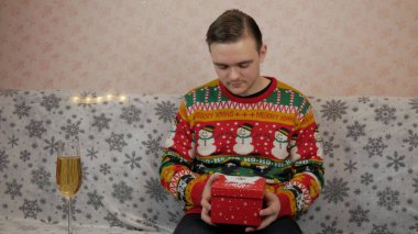 Yeni yıl tatili, genç bir adam bir hediye açar ve paketler, şampanya, yeni yıl hediyeleri, yeni yıl süslemeleri ve iyi bir ruh hali.