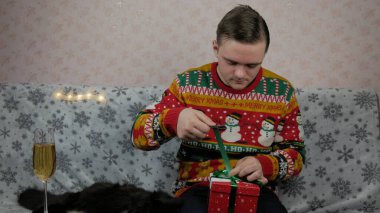 Yeni yıl tatili genç adam bir hediye açar ve paketler, şampanya, yeni yıl hediyeleri, yeni yıl süsleri ve iyi bir ruh hali ve siyah bir kedi.