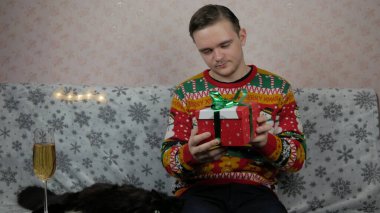Yeni yıl tatili genç adam bir hediye açar ve paketler, şampanya, yeni yıl hediyeleri, yeni yıl süsleri ve iyi bir ruh hali ve siyah bir kedi.