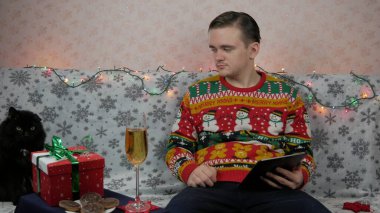 Yeni yıl tatili, genç bir adam bir hediye açar ve paketler, şampanya, yeni yıl hediyeleri, yeni yıl süslemeleri ve aile ile bir sohbet, online tablet